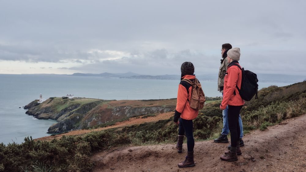 three people looking at the sea standing on a cliff path