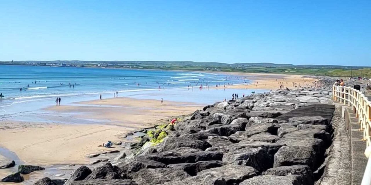 Lahinch beach on a sunny day, bright blue water, lots of sand and big boulders