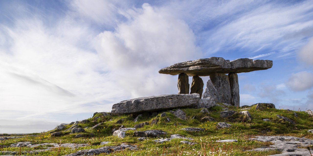 The Burren Poulnabrone Stone Portal Tomb/Dolmen atop of a small hill surrounded by grass and blue skies with some clouds 