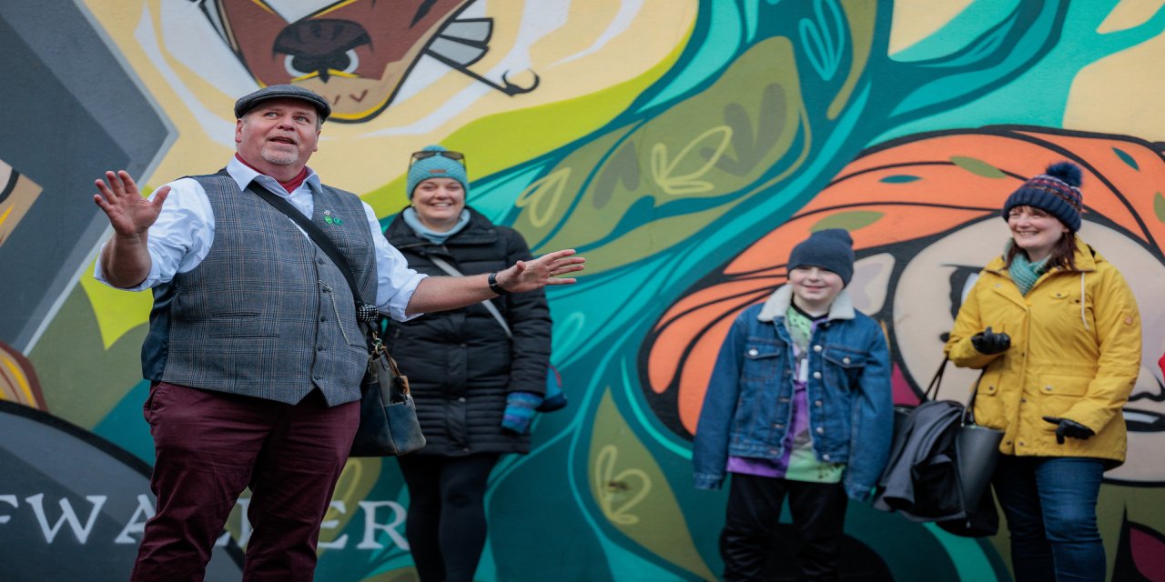 Graffiti wall with bue orange and green paint. Man with hat talking to a group of people 