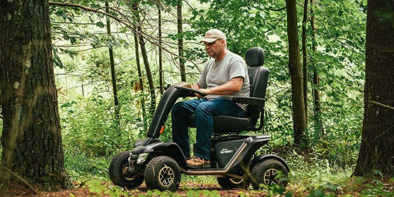 Man on mobility scooter driving along a trail in a green forest